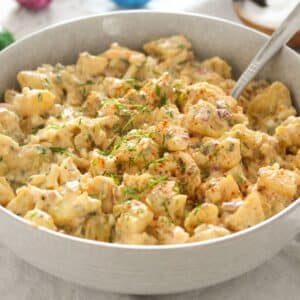 bowl with potato salad with dill pickles sprinkled with chives.