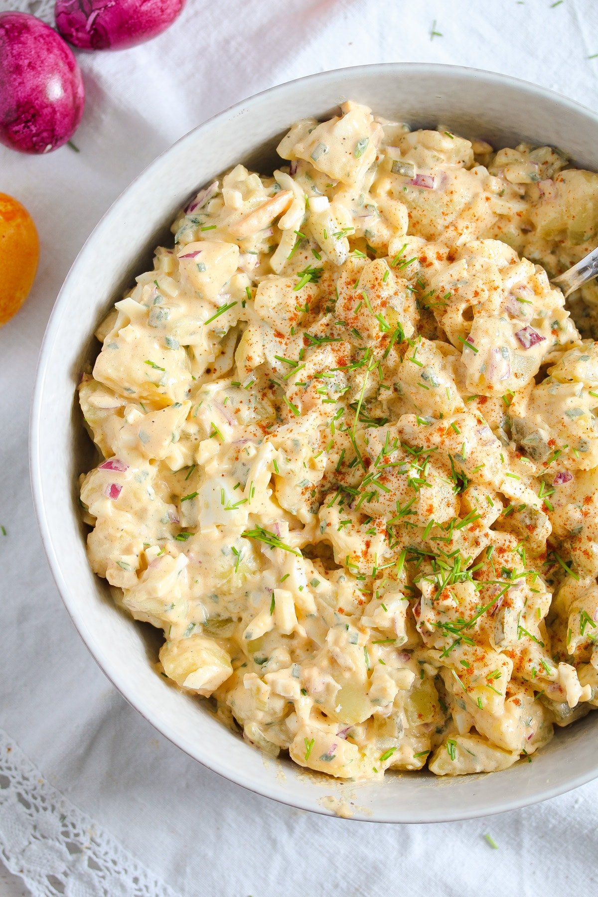 creamy deviled egg potato salad with pickles in a white bowl