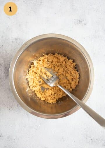 crushing egg yolks with a fork in a metal bowl.