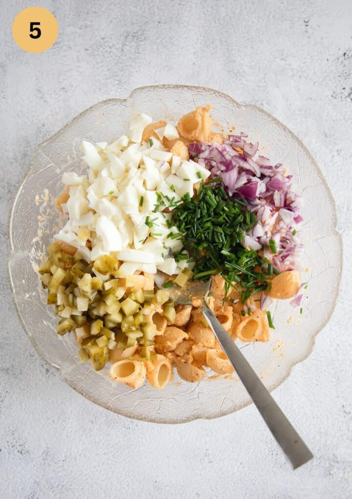 chopped ingredients for making pasta salad in a bowl: macaroni, egg whites, onions, chives, pickles.