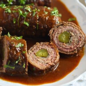 german beef roulades served in sauce and cut into several slices showing the gherkin inside.