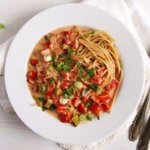 green onion pasta with red peppers and cream cheese sauce served over spaghetti on a large pasta plate.