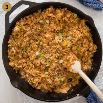 fried rice with kimchi, bacon and gochujang stirred with a wooden spoon in a skillet.