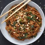 peanut butter spinach noodles tangled in a bowl and two chop sticks.