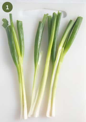green onions split lengthwise on a cutting board and ready for roasting.