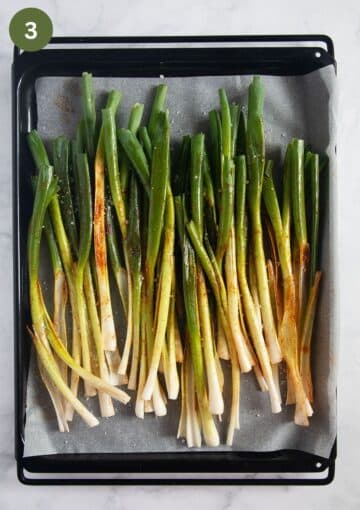 many green onions or scallions crowded on a baking sheet and ready to roast.