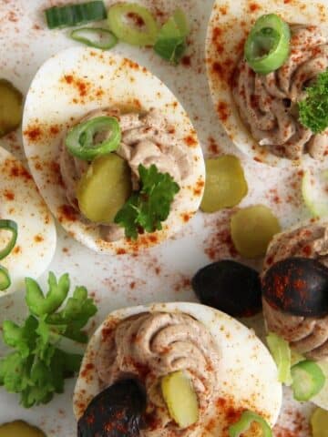 romanian deviled eggs filled with liver pate and garnished with olives and pickles.