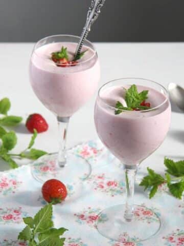 romanian strawberry foam or spuma de capsuni in two wine glasses decorated with mint and fresh strawberries.