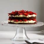 layered strawberry brownie cake on a high cake platter.