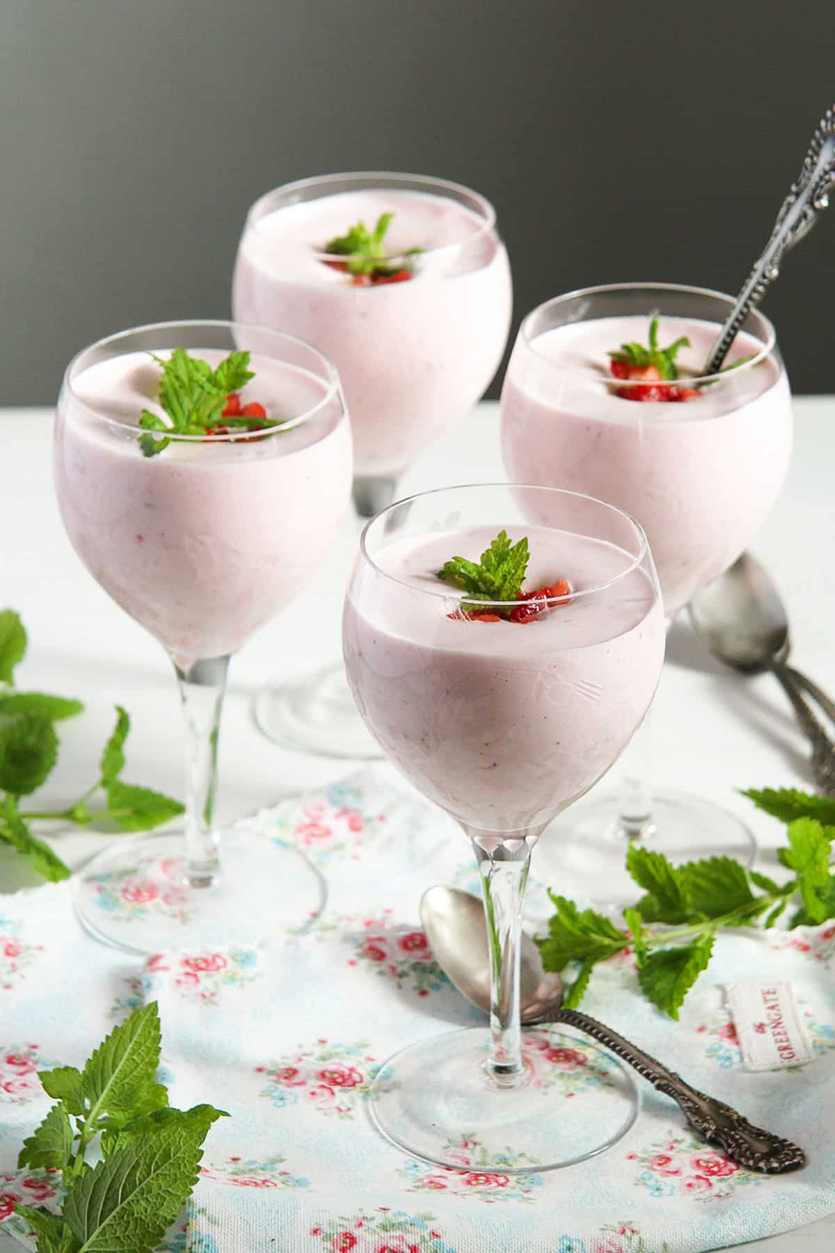 four glasses full of strawberry foam, garnished with fresh strawberries and mint.