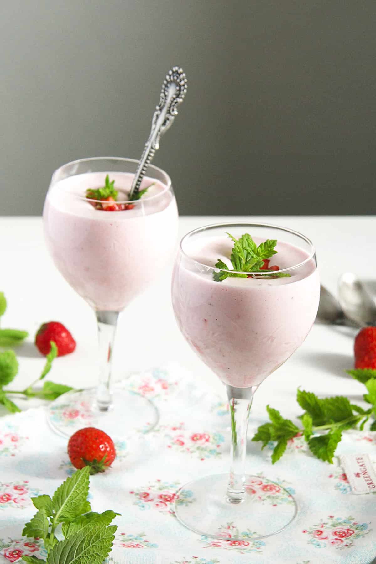 two glasses with strawberry foam, strawberries and mint leaves around them.