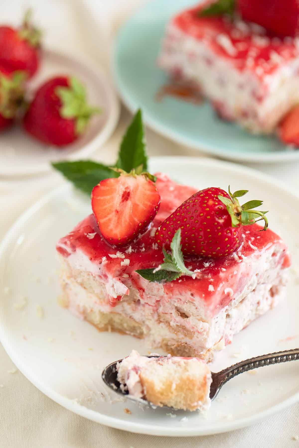 taking a piece of strawberry tiramisu with a small spoon from a square piece.