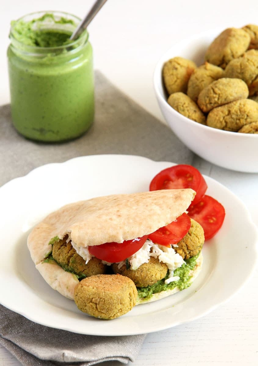 a falafel sandwich with tomatoes, a small of wild garlic pesto and more falafel behind it.