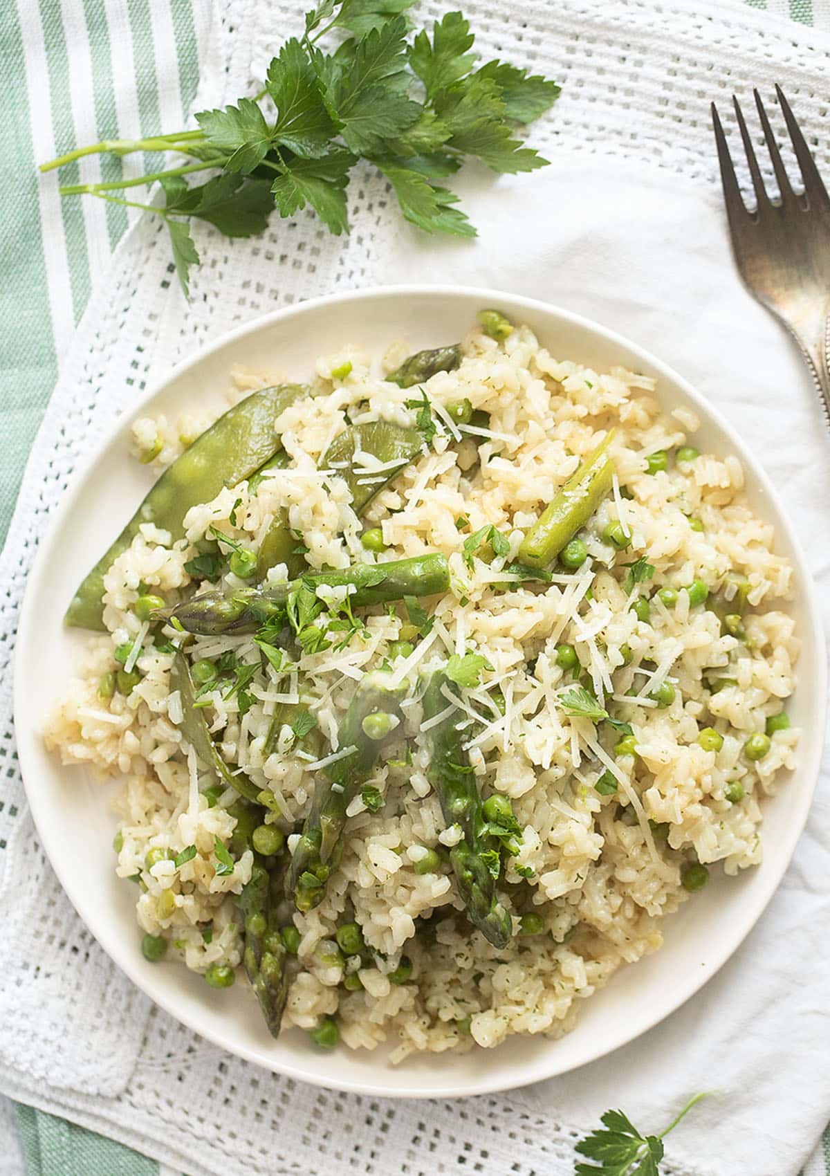 overhead view of a white plate with risotto with peas and fresh asparagus.