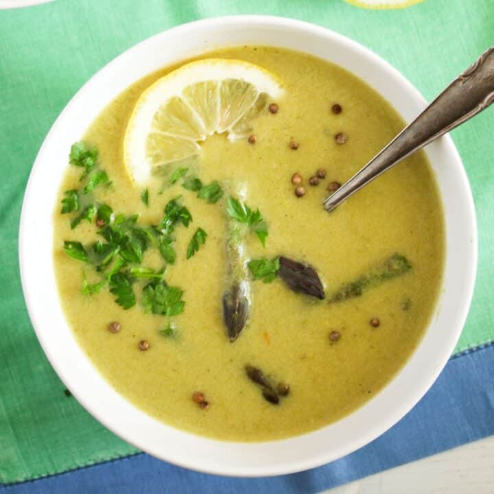 bowl of asparagus soup with milk, lemon and parsley inside.
