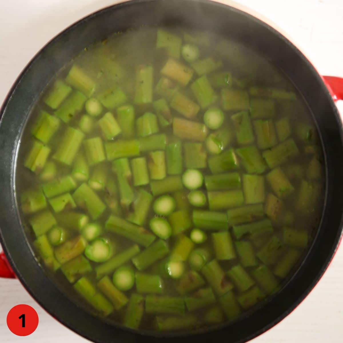 chopped green asparagus cooking in a red pot.