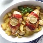 bacon-wrapped chicken with herbs and potato cubes in a baking dish.