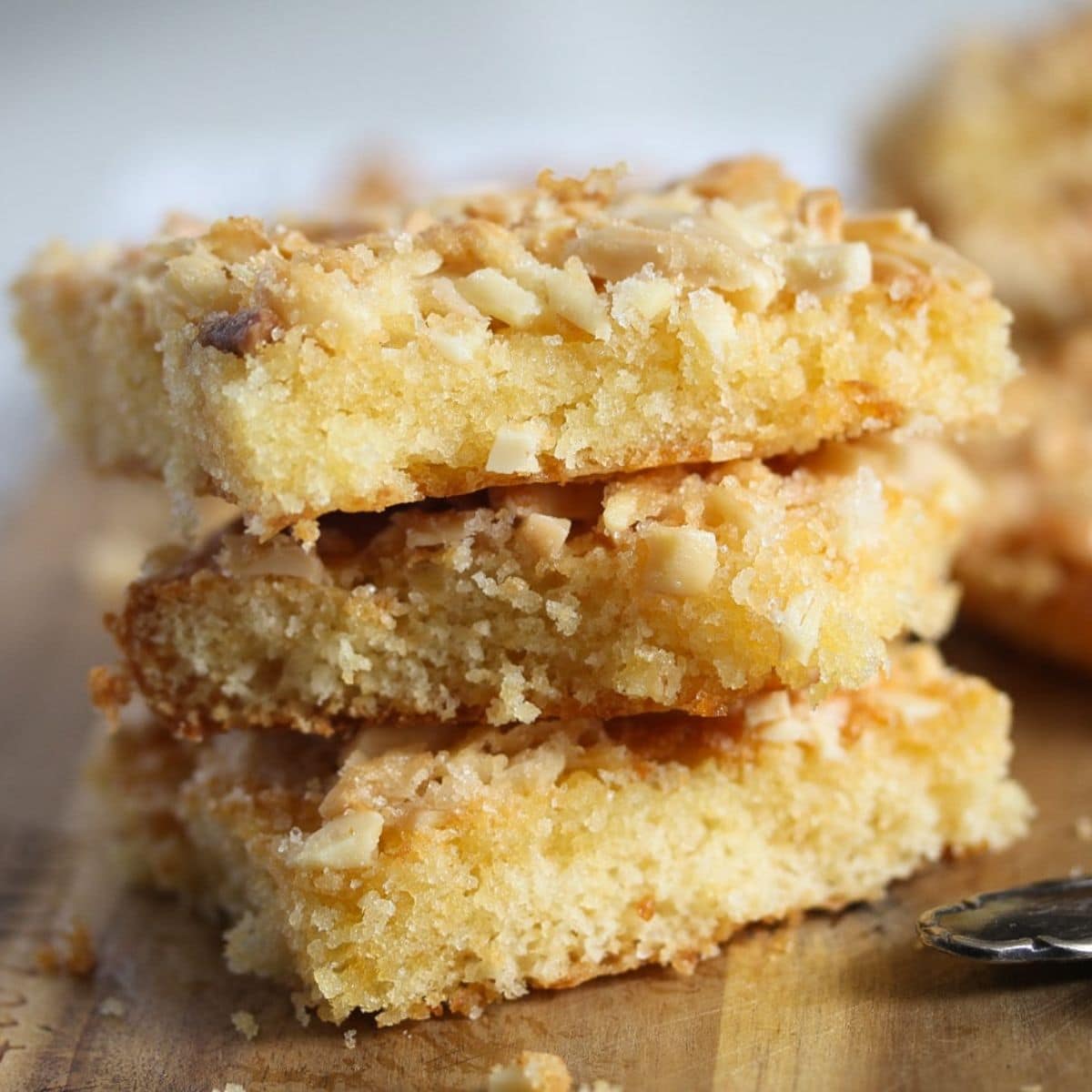 three square pieces of german blitzkuchen with almonds on a wooden board.