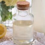 a small bottle of elderflower syrup, half a lemon and a bunch of elderflowers in a vase.