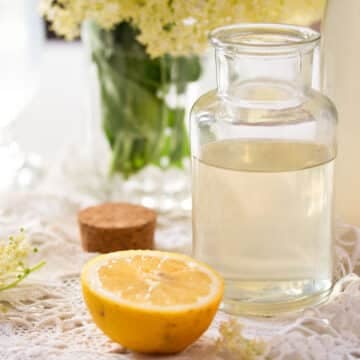homemade elderflower syrup in a small bottle and a lemon half.