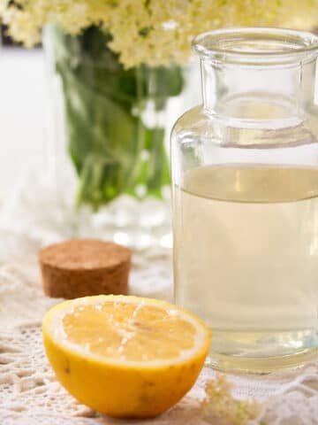 homemade elderflower syrup in a small bottle and a lemon half.