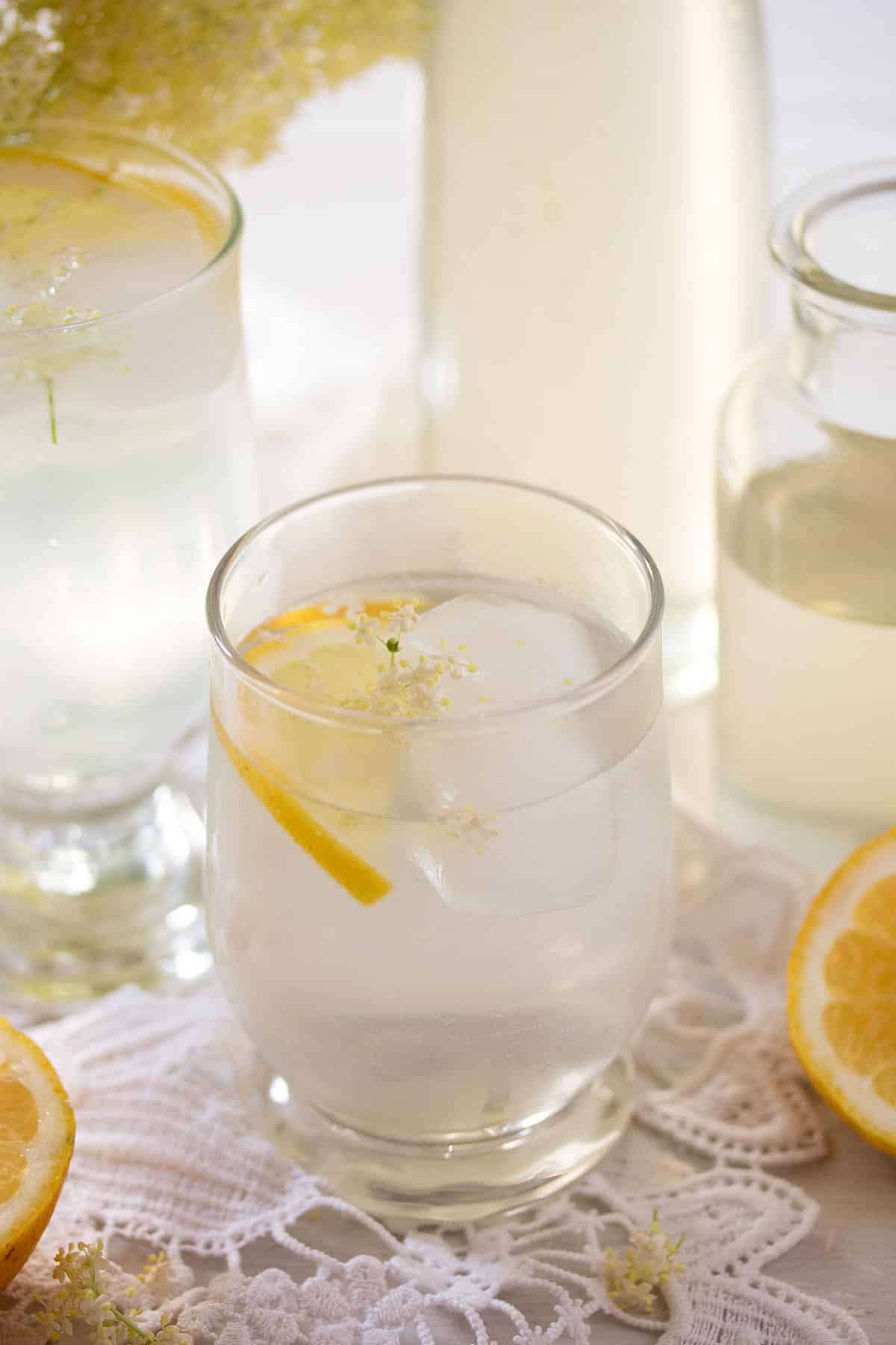 elderflower syrup mixed with water and a slice of lemon in a jam, a bottle of syrup behind it.