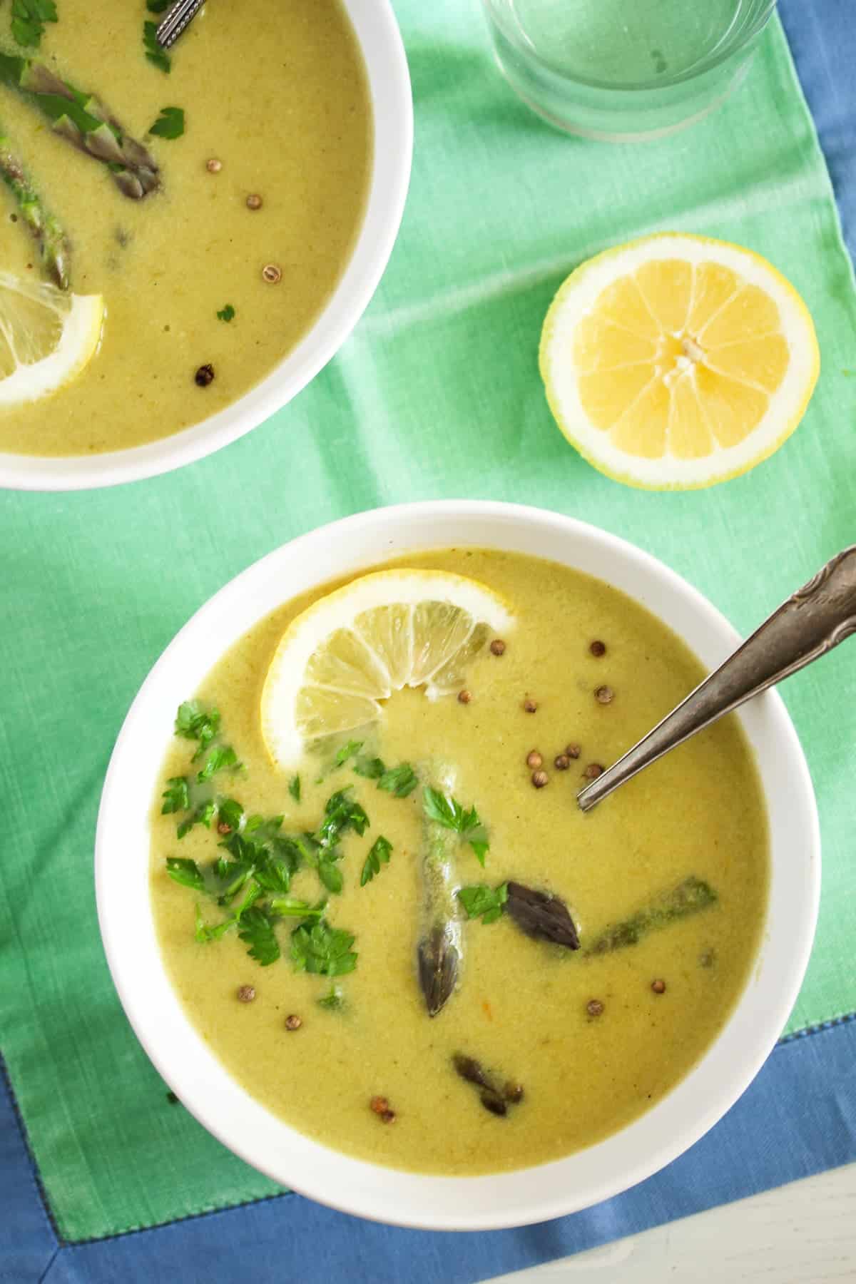 two bowl of soup with green asparagus on a green table cloth with blue margins.