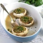 three herb-stuffed mushrooms in a baking dish with a spoon.