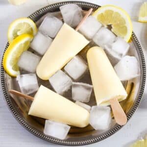 three homemade lemon popsicles, ice cubes, and lemon slices on a large silver plate.