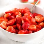 macerated strawberries in a white bowl with a spoon in it.