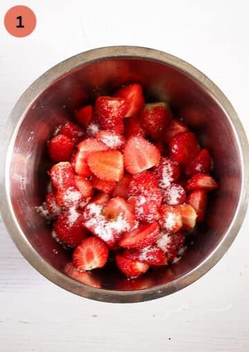 halved strawberries mixed with granulated sugar in a metal bowl.