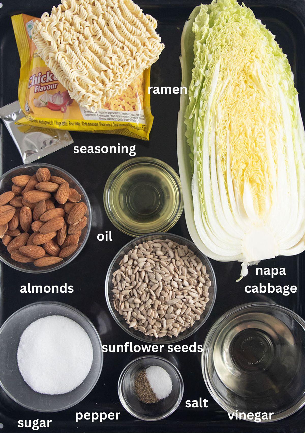 labeled ingredients fo rmaking salad with napa cabbage, ramen noodles, almonds and sunflower seeds.