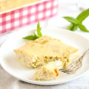 nigella#'s baked rhubarb custard sliced on a plate, mint leaves behind and a pink casserole dish behind it.