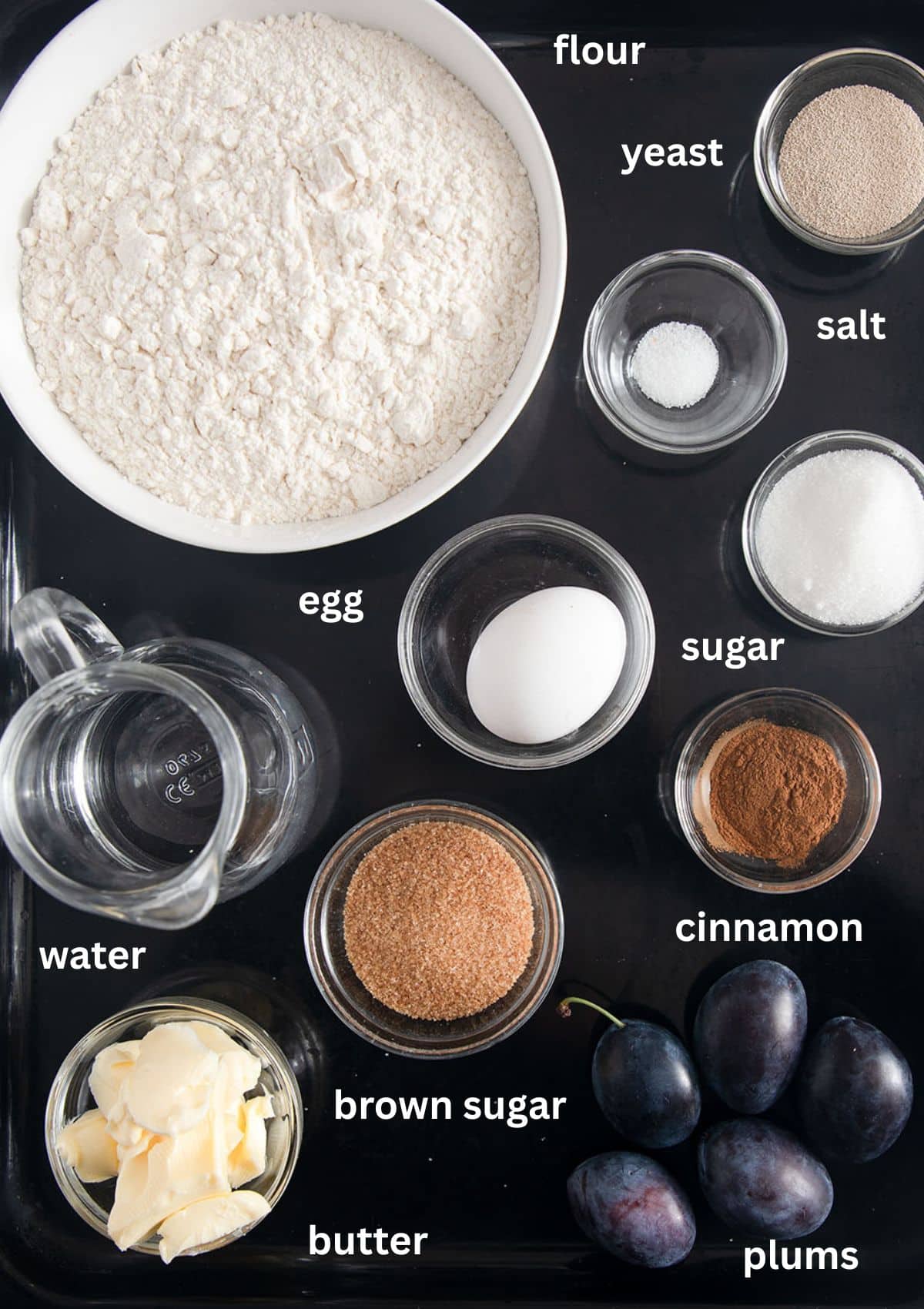 labeled ingredients for making plum bread with yeast, cinnamon, sugar, flour, butter.