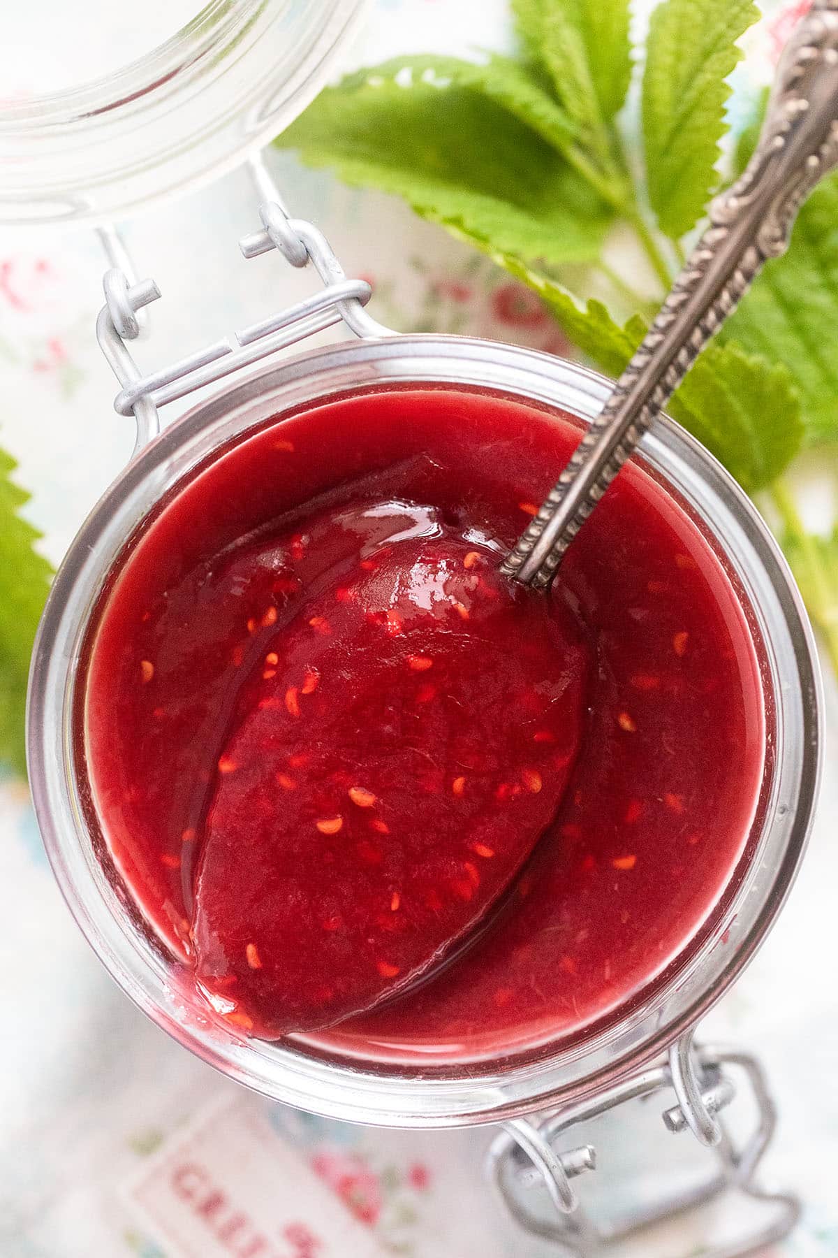 overhead view of a jar with vibrant red jam with a spoon in it.