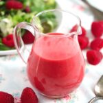 berry vinaigrette in a small jug with salad in the back