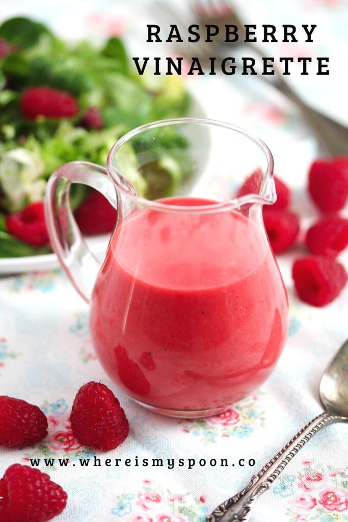 berry vinaigrette in a small jug with salad in the back