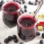 two small jars with rhubarb blueberry jam and fresh blueberries around them.