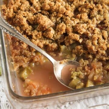 rhubarb apple crisp in a baking dish with a spoon and juices.