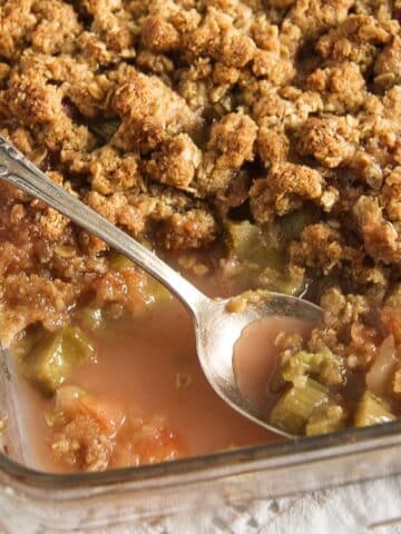 rhubarb apple crisp in a baking dish with a spoon and juices.