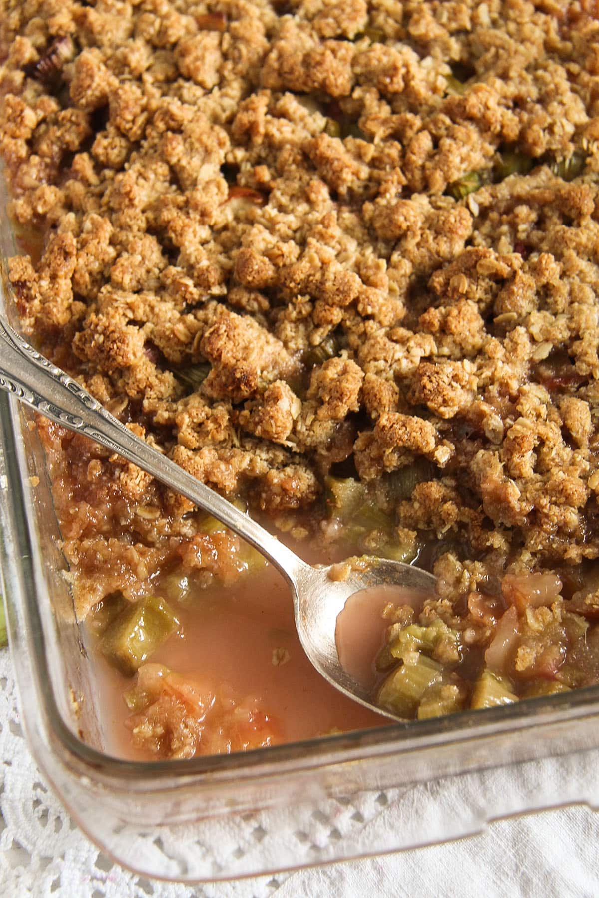 baking dish full of apple crisp with rhubarb with a spoon in it.