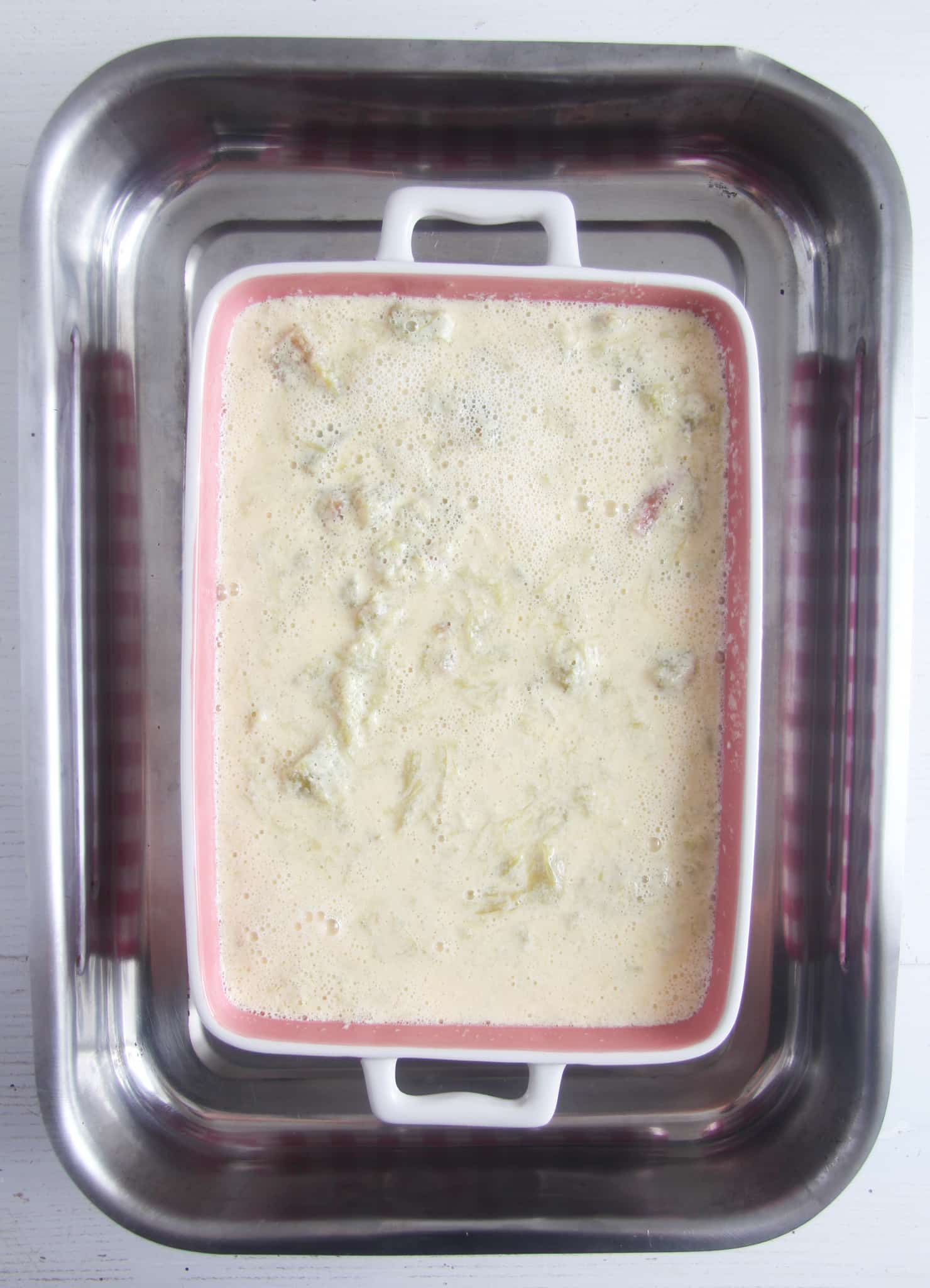 casserole dish containing rhubarb custard ready to baked in a larger baking dish filled with water.
