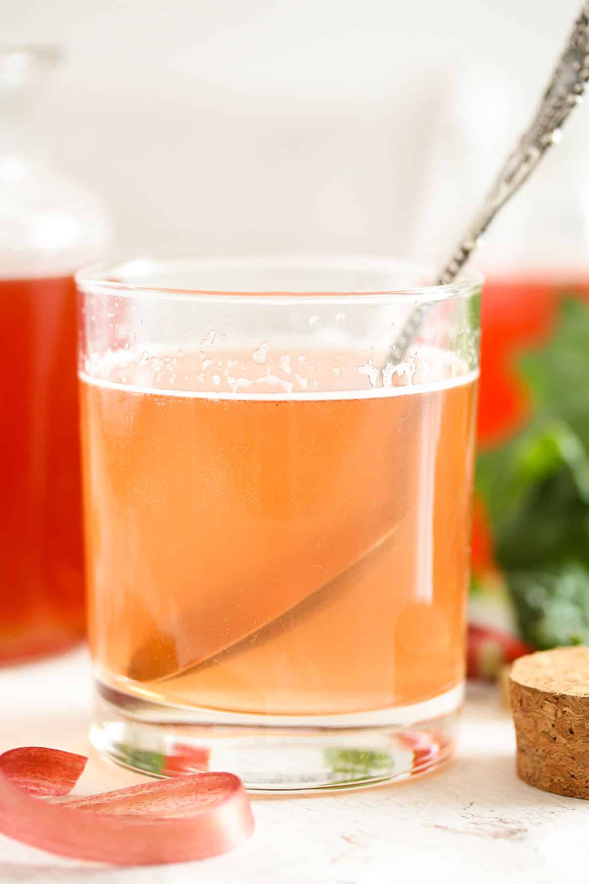 stirring rhubarb syrup with water in a glass.