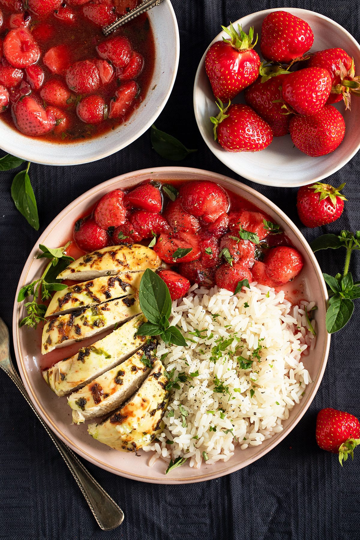 chicken breast with savory strawberry sauce and rice, bowls with more sauce and fresh strawberries near it.