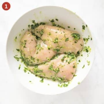 three chicken breast in parsley marinade in a bowl.