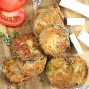 pan fried zucchini with flour on a wooden board with tomato and feta cheese slices.