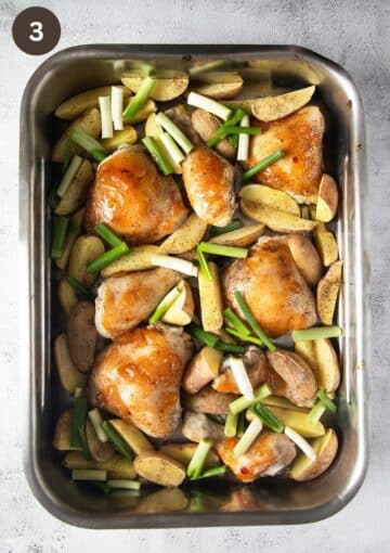 halve-baked chicken with mango, potatoes and spring onions in a roasting pan.