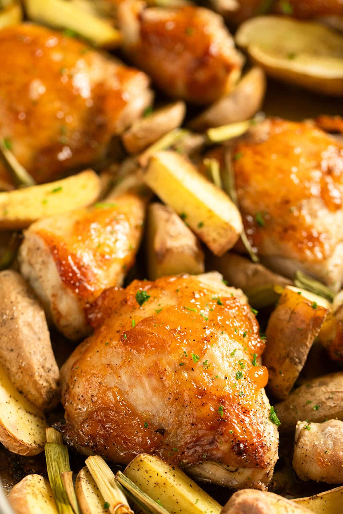 mango chicken thighs baked with potato wedges and green onions on a baking sheet.