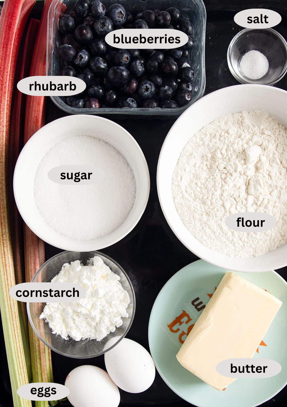 labeled ingredients for making pie with blueberries, rhubarb, butter, eggs, flour, sugar, and cornstarch.