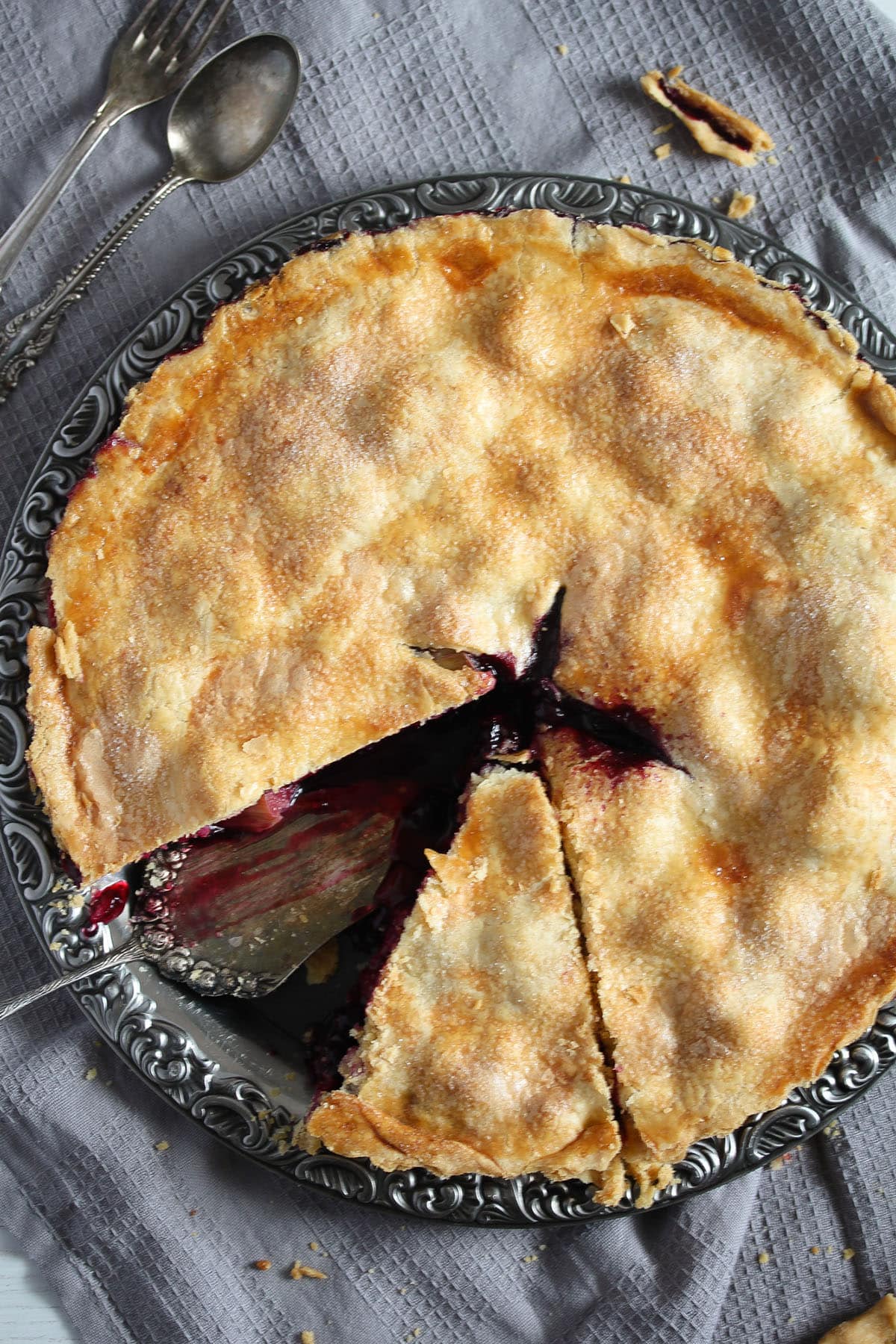 a rhubarb and blueberry pie with a slice cut off on a round platter.